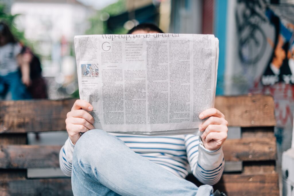Eine Person sitzt auf einer Bank und liest eine Zeitung. Wenn Sie mit Ihrer Pressemitteilung erfolgreich sind, dürfen Sie auf einen Artikel in der Lokalzeitung hoffen.