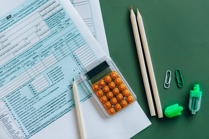 Ein Taschenrechner mit Stiften und einer unausgefüllten Steuererklärung liegt auf einem grünen Tisch. Für Vereine ist wichtig, dass alle Einnahmen und Ausgaben den korrekten steuerlichen Tätigkeitsbereichen zugeordnet werden.
